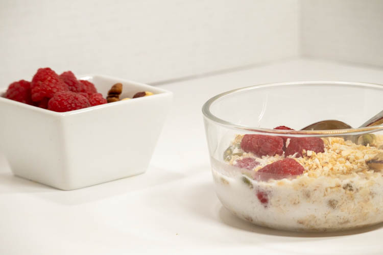 Maply Nut Granola with berries in clear bowl beside a bowl of nuts and berries